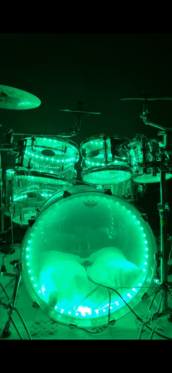 A clear acrylic drum kit illuminated in green by DrumLight